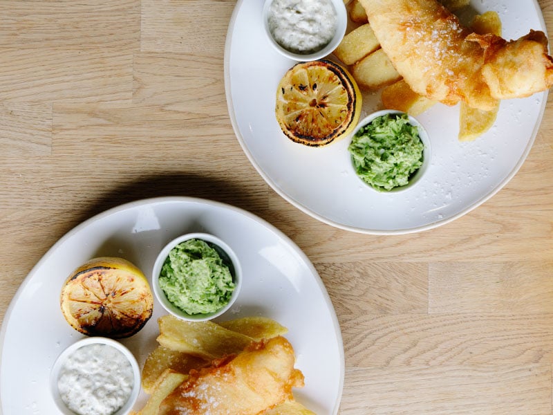 overhead view of fish and chips with mushy peas and charred lemon