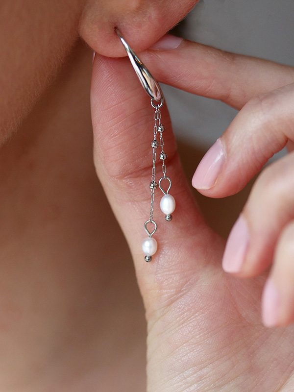 Close up of model wearing drop stainless steel and freshwater pearl earrings