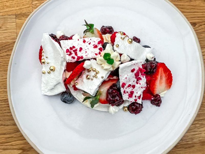 Plates of Eton Mess with Chantilly cream, coulis, and winter berries
