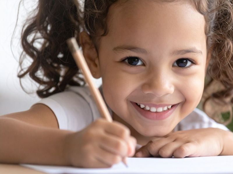 little girl holding a pencil to write and smiling